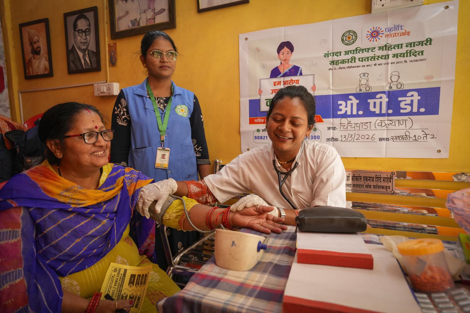 A member having her blood pressure checked by a doctor at the hub, with a health worker standing behind